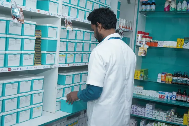 A team member arranges items in the pharmacy's aqua storage drawers. — Parsagarh Bazar