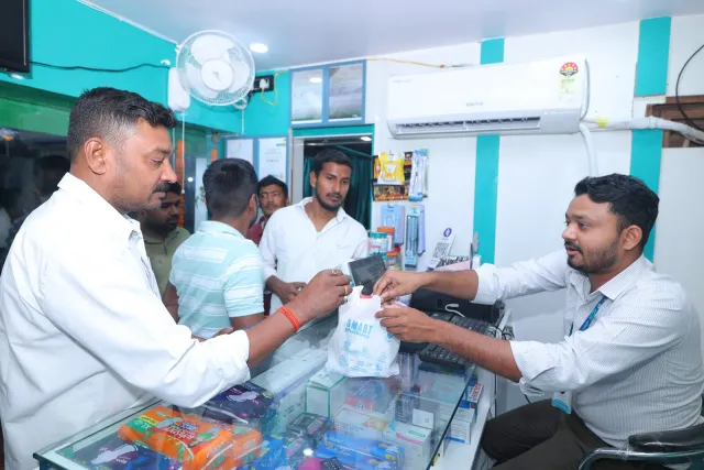 A pharmacy bag is handed across the counter with a friendly exchange. — Jamalpur, Munger