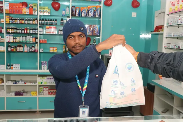 A packed pharmacy bag is handed across the counter. — Ramnagri Store